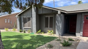 A building with a grey exterior, a red door, and a well-maintained lawn with small plants and a tree. - New family retreat w/private heated pool and hot tub (Chandler)