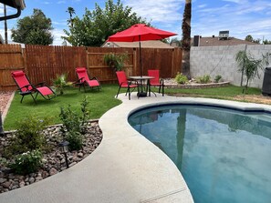 A backyard with a swimming pool, red lounge chairs, a red umbrella, and a wooden fence. - New family retreat w/private heated pool and hot tub (Chandler)