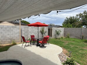 A patio area with a concrete table and chairs, a red umbrella, and string lights. - New family retreat w/private heated pool and hot tub (Chandler)