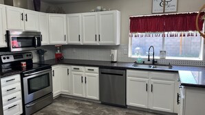 A modern kitchen with white cabinets, stainless steel appliances, a granite countertop, and a window with a red valance. - New family retreat w/private heated pool and hot tub (Chandler)