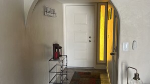 A hallway with a white door, a welcome sign, a small table with a lantern, and a glass table with a light fixture. - New family retreat w/private heated pool and hot tub (Chandler)