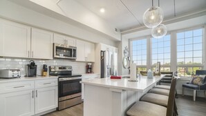Une cuisine moderne avec des meubles blancs, des appareils en acier inoxydable et un grand îlot central doté de tabourets.