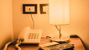 Una habitación de hotel con una mesita de noche que tiene un teléfono, una lámpara y un control remoto.