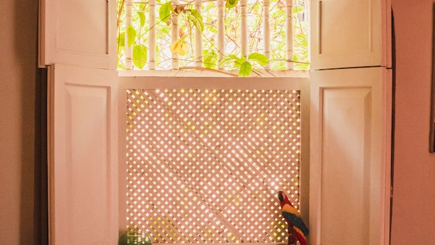Una habitación con una cama, un ventanal con celosía y una pequeña mesa con una vela.