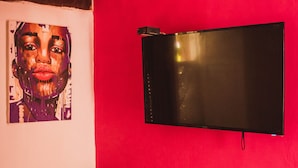 Una habitación con una silla color aguamarina, un taburete de madera y un televisor de pantalla plana montado en una pared roja.