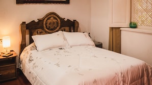 Una cama bien tendida con una colcha estampada y un cabecero de madera, junto a una mesita de noche con una lámpara.