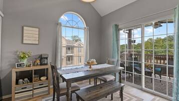 A dining area with a wooden table, chairs, and a bench. There is a window with a view of a house and trees.