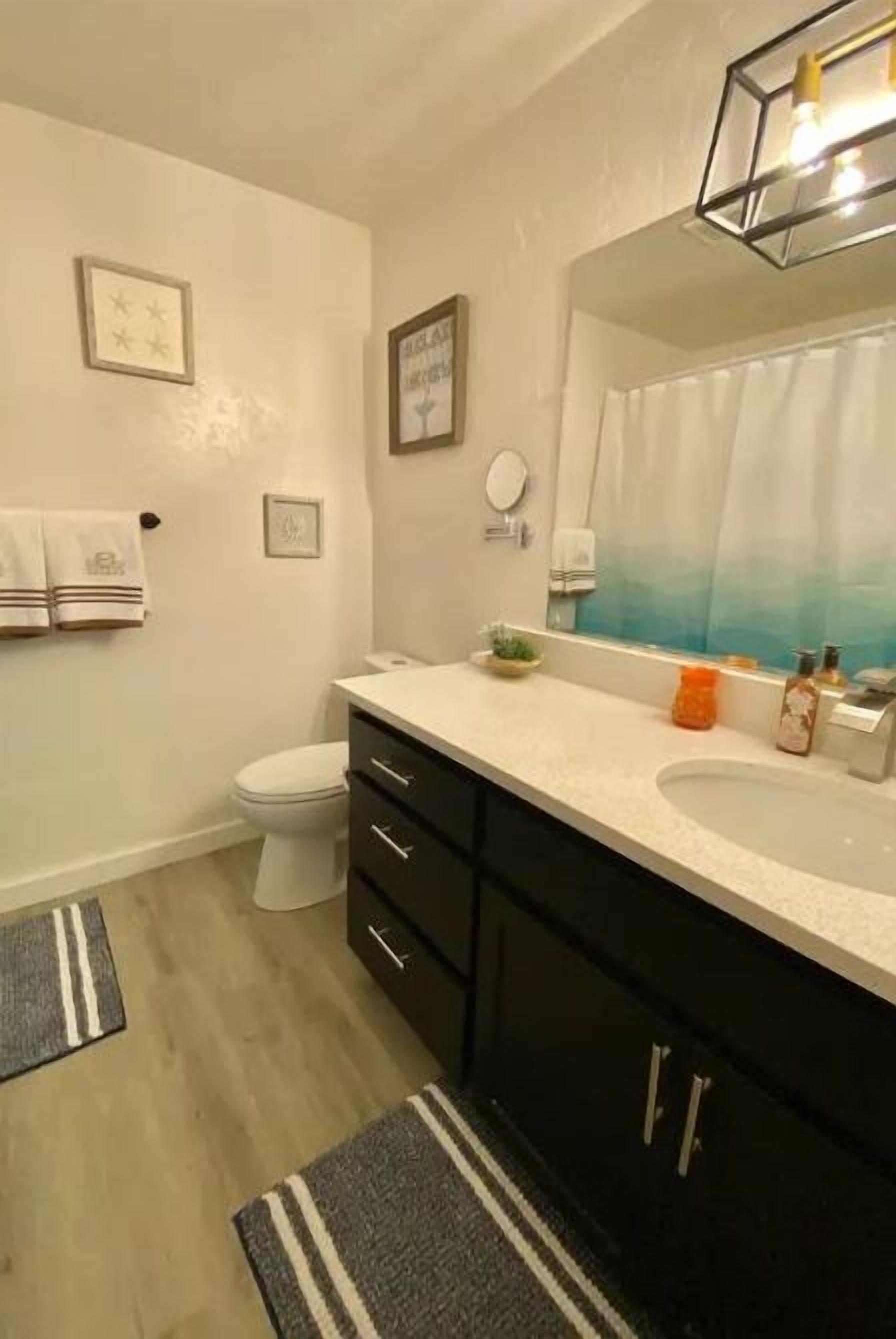 A bathroom with a white toilet, black cabinets, a white sink, and a mirror. There are two towels hanging on the wall and a shower curtain with a blue gradient.