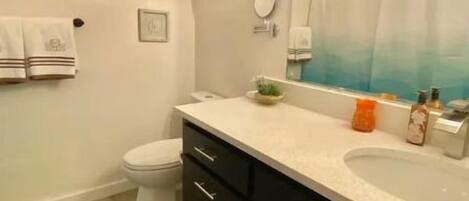 A bathroom with a white toilet, black cabinets, a white sink, and a mirror. There are two towels hanging on the wall and a shower curtain with a blue gradient.