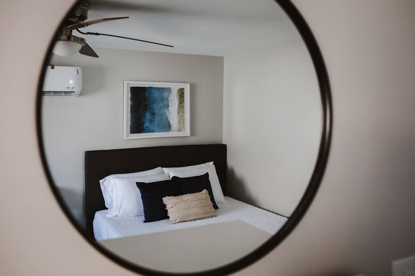 Een slaapkamer met een bed, een hoofdeinde, een wandairconditioner en een lijst met een abstract schilderij.