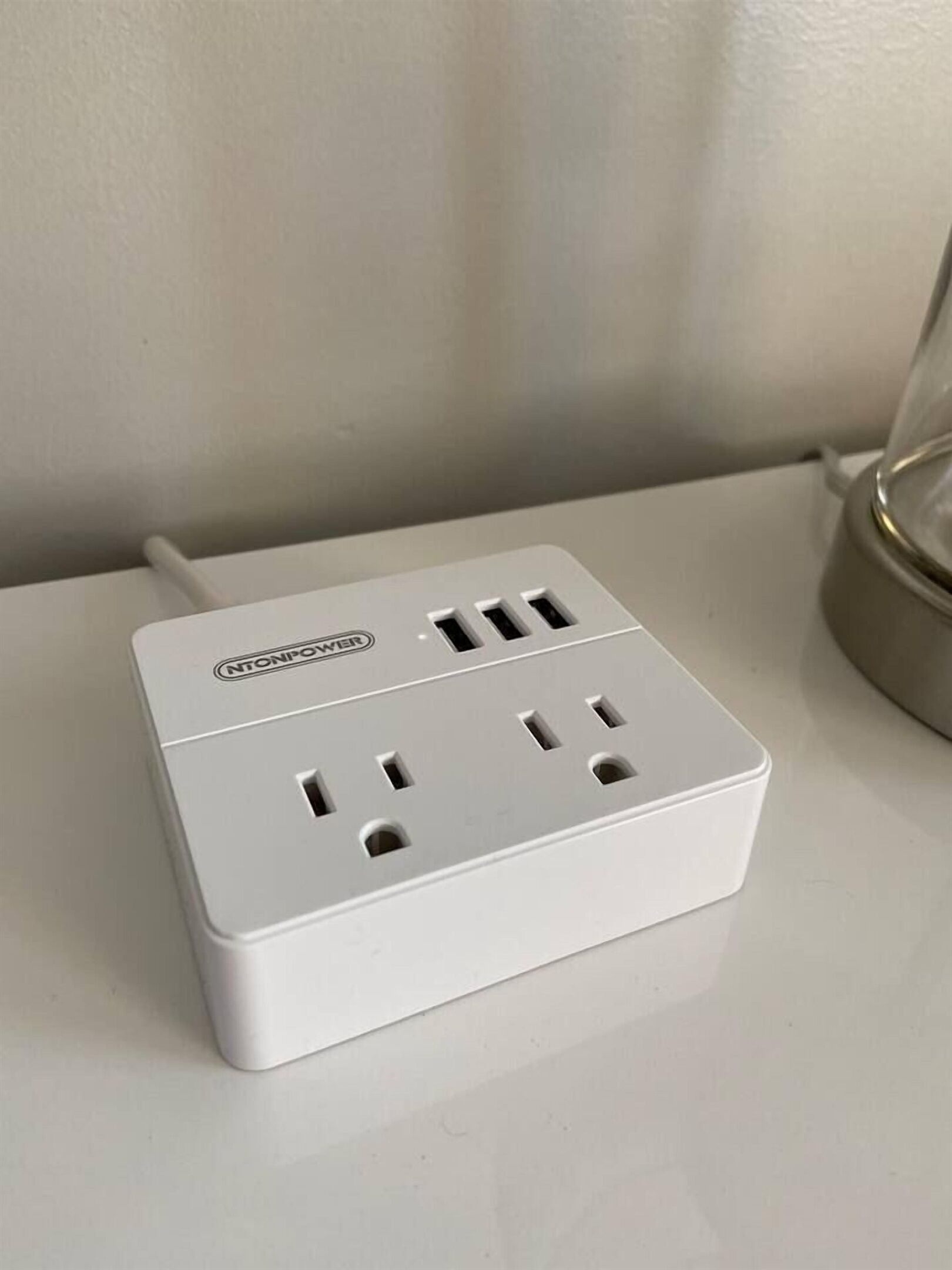 A white power strip with multiple outlets and a USB port, placed on a white surface.