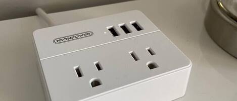 A white power strip with multiple outlets and a USB port, placed on a white surface.