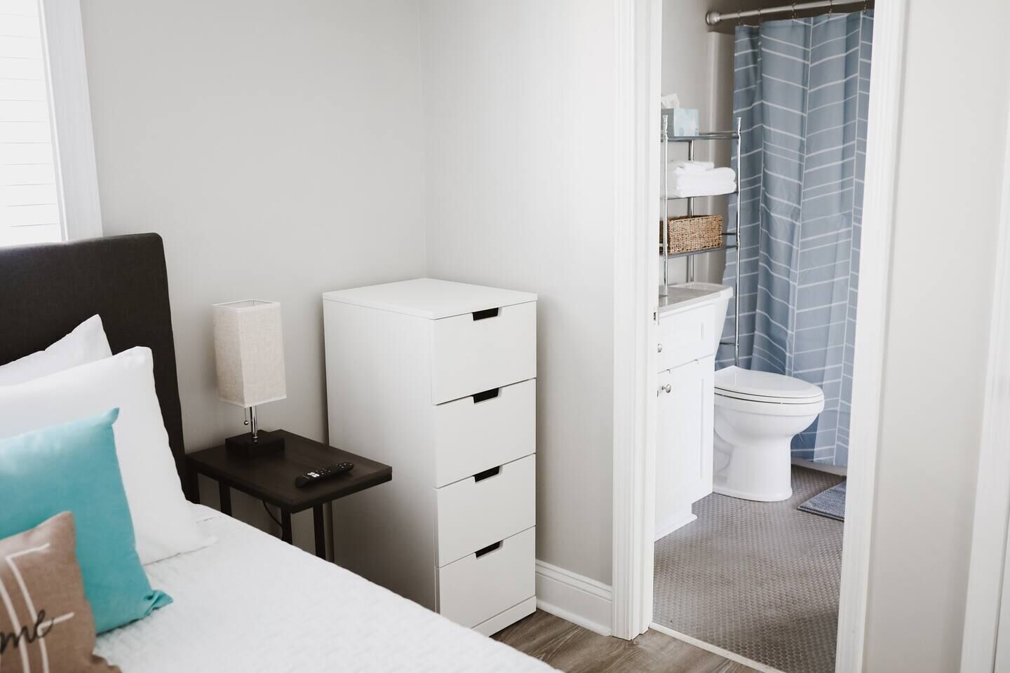 Un dormitorio con cama, mesita de noche, lámpara y un mueble blanco para guardar cosas.