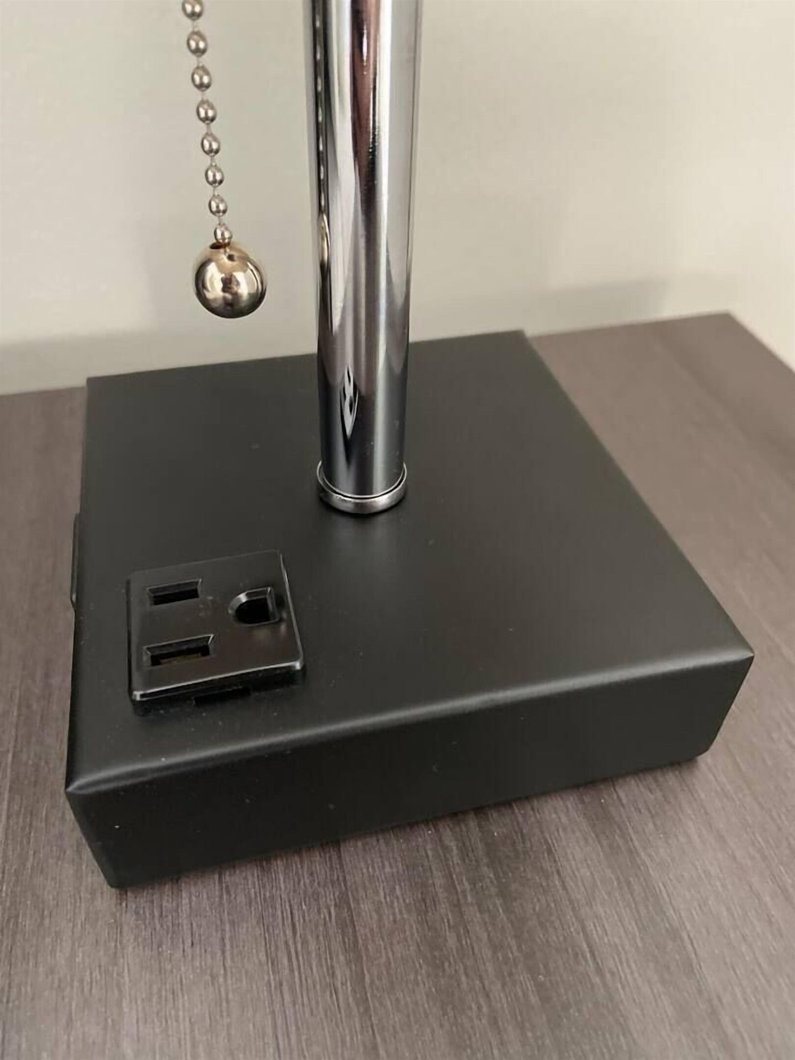 Een zwart, rechthoekig metalen object met een cilindervormige uitstulping en een ketting met een bolletje.