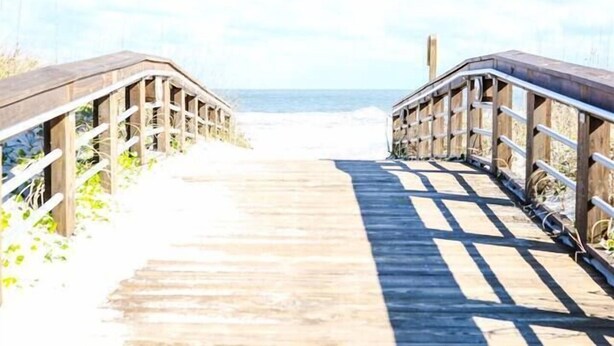 Una passerella di legno che conduce a una spiaggia, con cielo sereno.