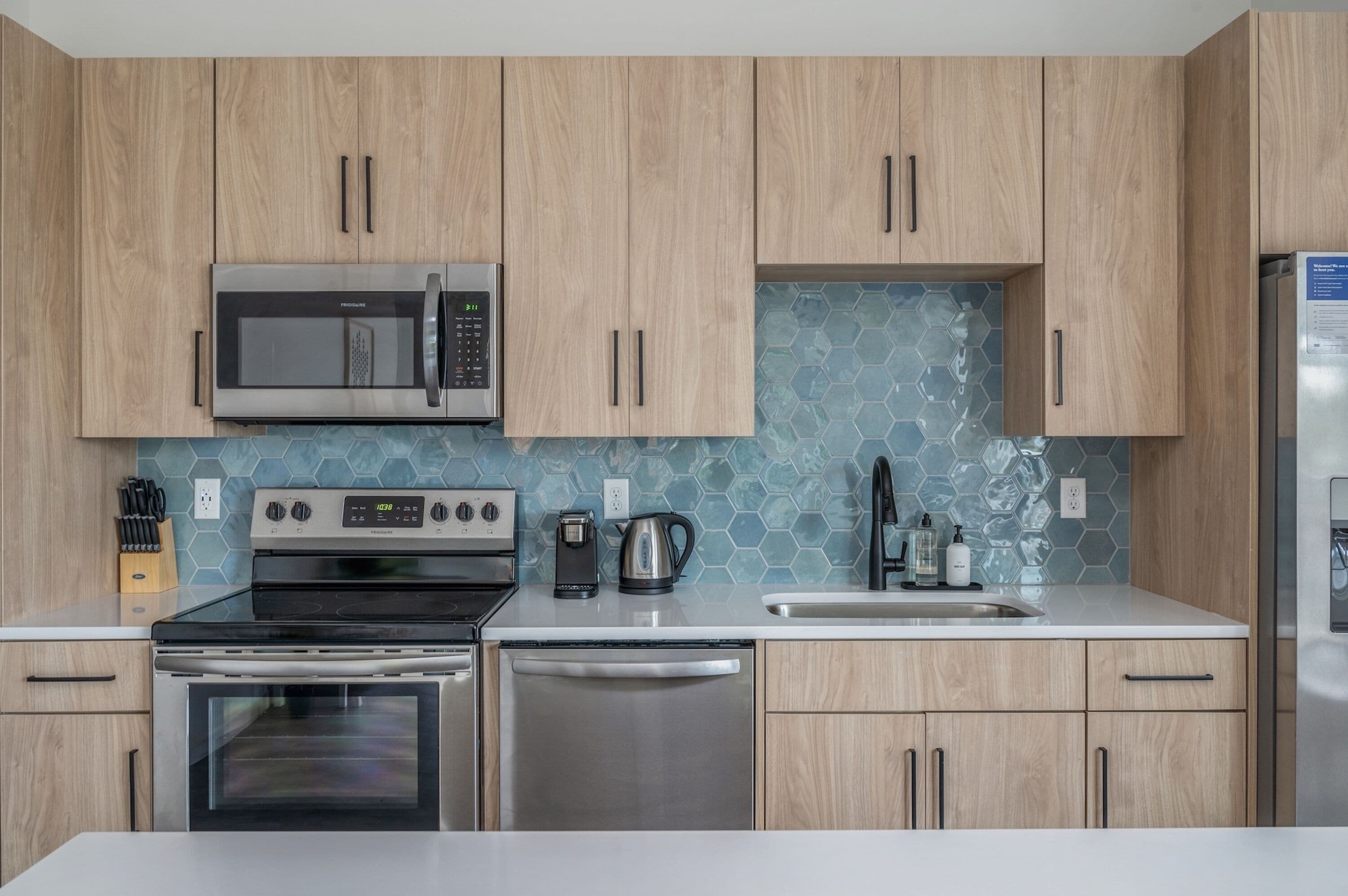 Eine moderne Küche mit Holzschränken, Edelstahlgeräten und einer sechseckigen Fliesenrückwand.
