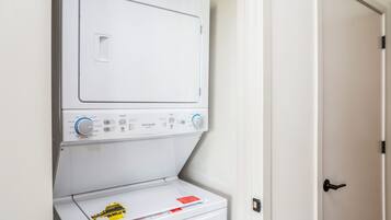 A front-loading washing machine with a control panel, a door, and a laundry basket with a yellow caution label.