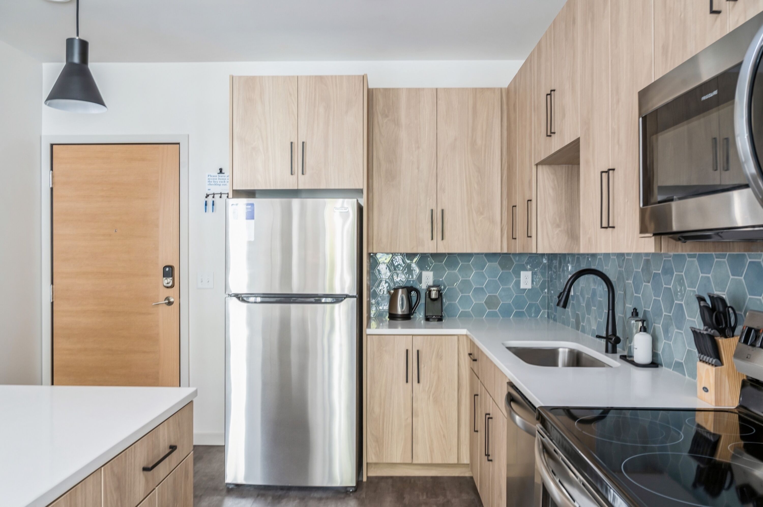 Una cocina moderna con armarios de madera, electrodomésticos de acero inoxidable, un grifo negro y salpicadero de azulejos.