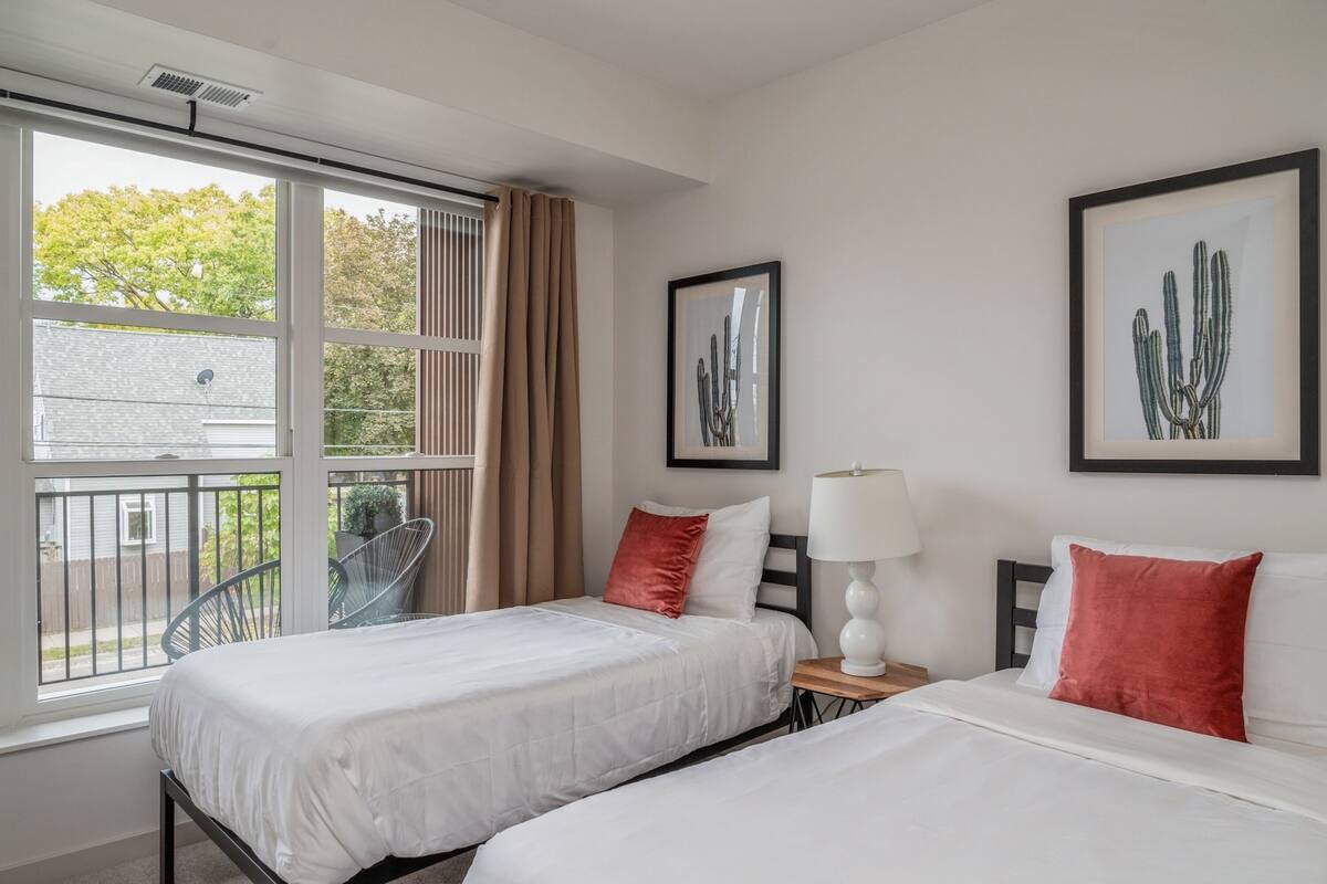 Habitación de hotel con dos camas, una ventana que da a un árbol y dos cuadros con imágenes de cactus en la pared.