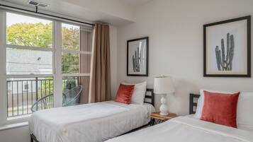 A hotel room with two beds, a window with a view of a tree, and two framed cactus pictures on the wall.