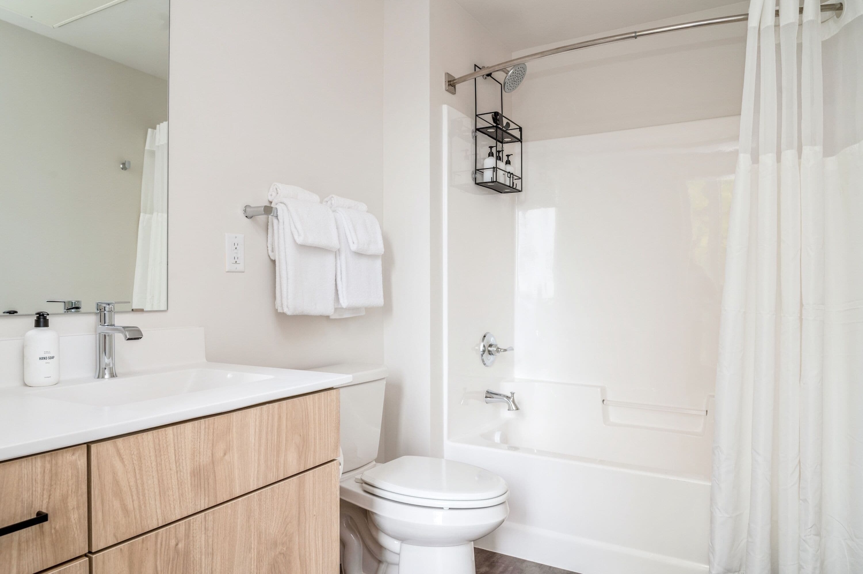A modern bathroom with a white sink, wooden cabinets, a toilet, and a shower with a glass door.
