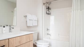 A modern bathroom with a white sink, wooden cabinets, a toilet, and a shower with a glass door.