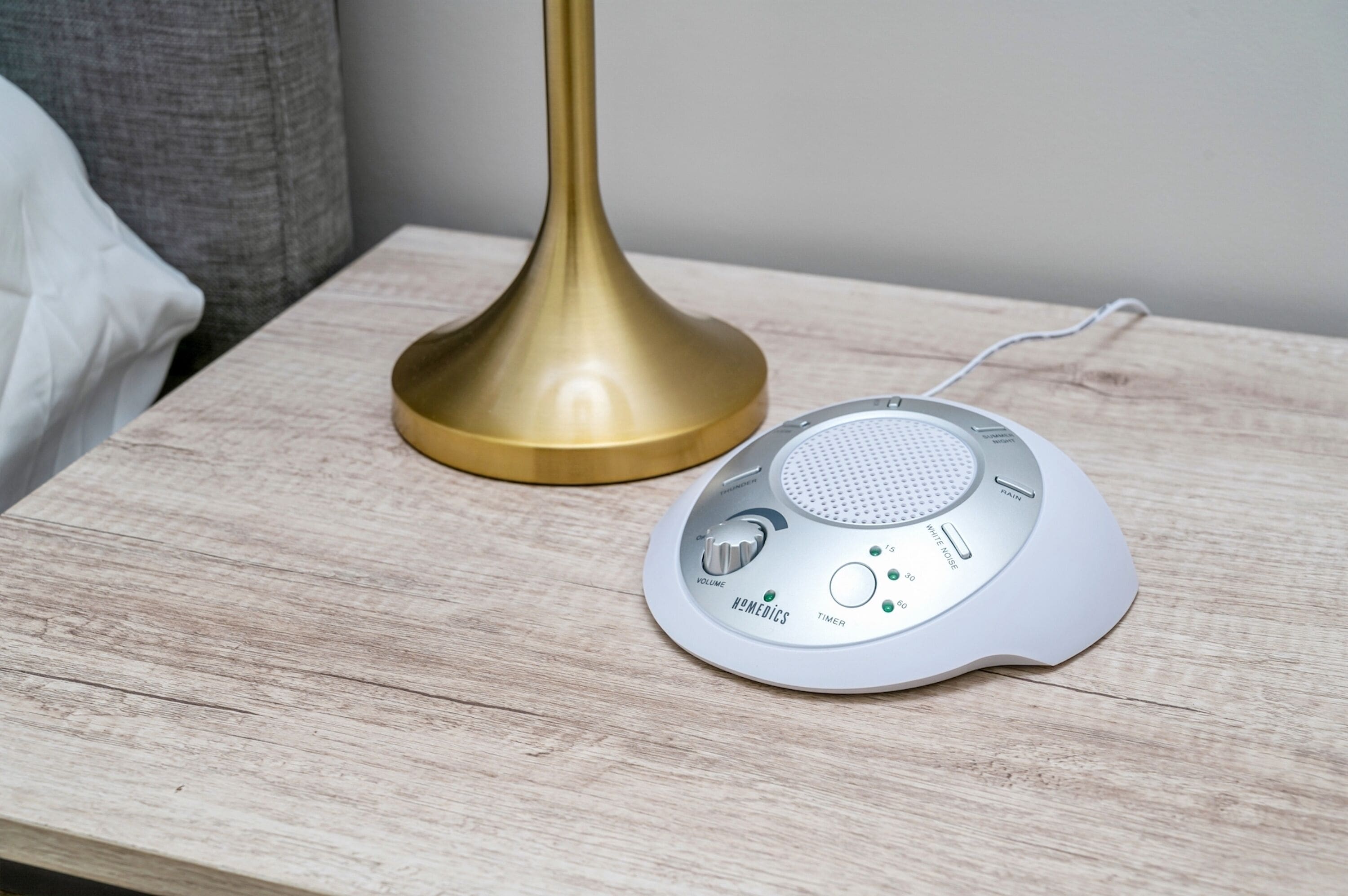 Een witte draagbare speaker met bediening voor volume en timer op een houten nachtkastje.