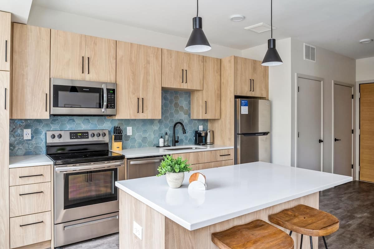 Una cocina moderna con armarios de madera, electrodomésticos de acero inoxidable, una isla grande e iluminación colgante.