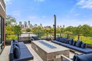 Een terras op het dak met uitzicht op de skyline van de stad, buitenmeubels en een modern vuurkorf.