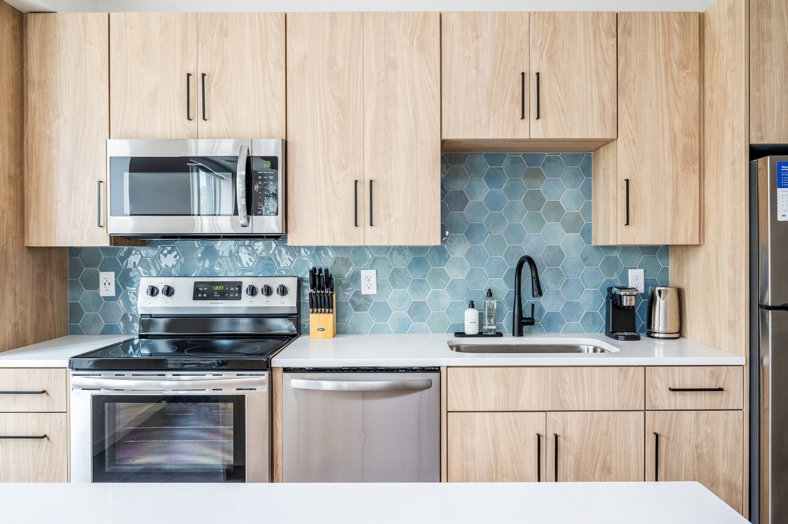 A modern kitchen with wooden cabinets, stainless steel appliances, a microwave, stove, dishwasher, and a sink with a faucet.