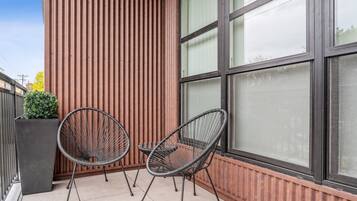 To sorte stole med metalstel på en fliseterrasse ved siden af en bygning med lodrette træpaneler og store vinduer.