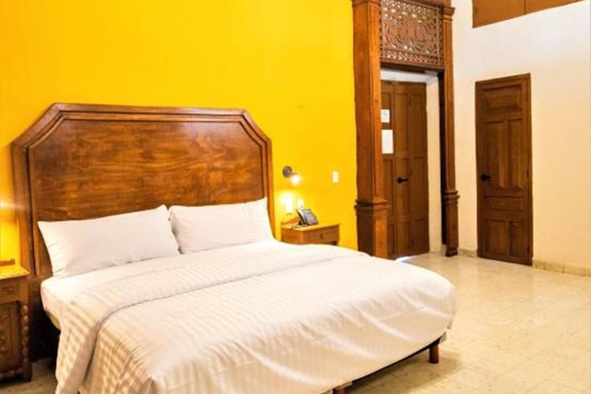 A large bed with a wooden headboard, a nightstand with a lamp, and a ceiling fan in a room with yellow walls and wooden doors.