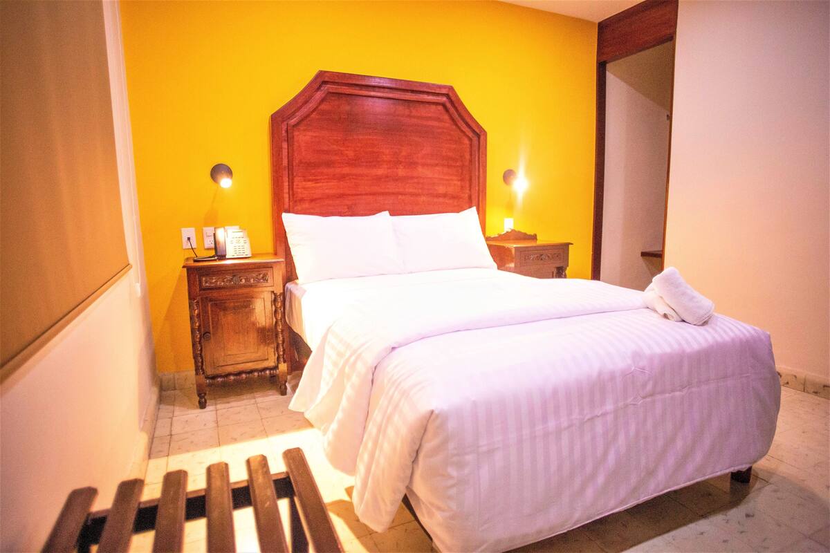 A neatly made bed with white linens, a wooden headboard, and two bedside lamps.