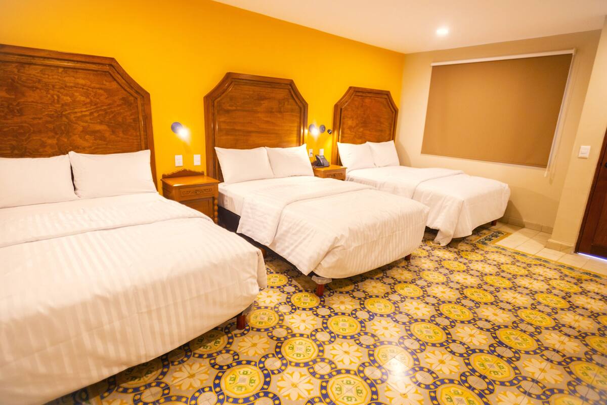 A hotel room with three beds, a patterned floor, and wooden headboards.
