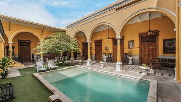 A courtyard with a swimming pool, outdoor seating, and a tree.
