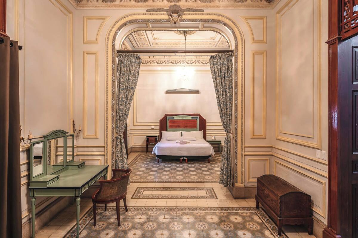 A bedroom with a bed, a desk, a chair, and a small cabinet.