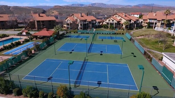 A tennis court complex with multiple courts, a pool, and residential buildings in the background.