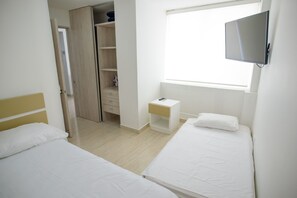 Ein Schlafzimmer mit zwei Betten, einem Kleiderschrank, einem Nachttisch, einem Fernseher und einem Fenster.