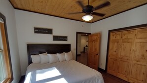 Ein Schlafzimmer mit einem großen Bett, Holzboden und Deckenventilator. An der Wand befinden sich zwei Schilder und ein Holzschrank.