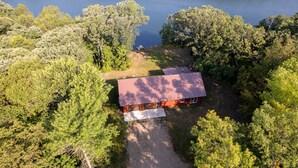 Eine Vogelperspektive zeigt eine Hütte, umgeben von dichtem Wald, mit einem See im Hintergrund.