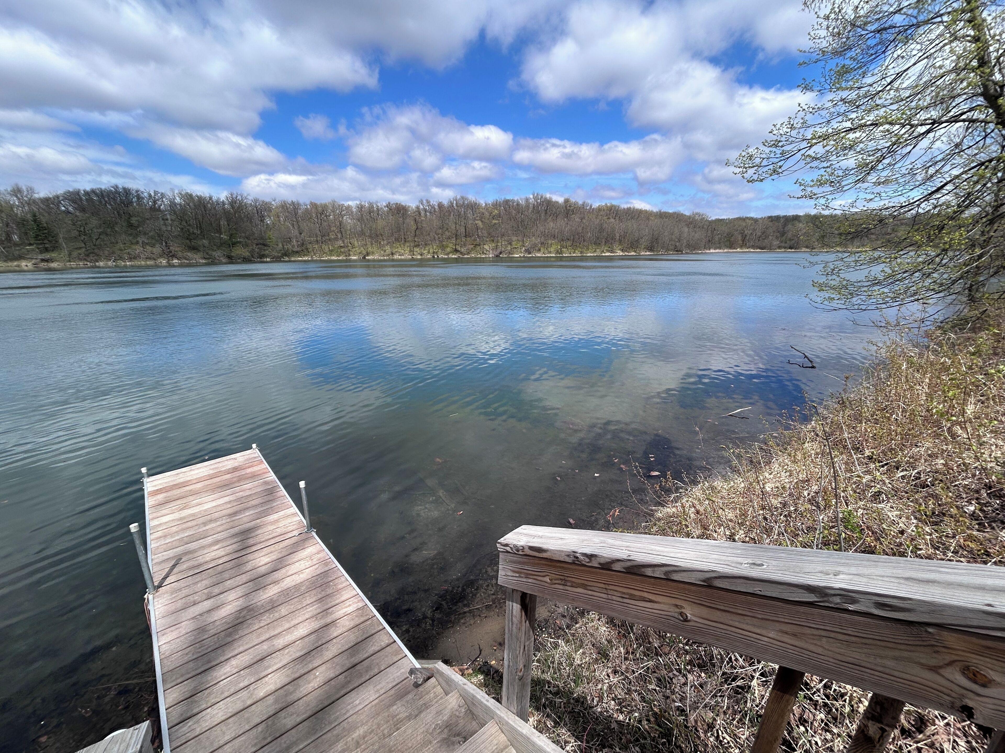A wooden dock extending into a calm lake with a forested shoreline in the background.