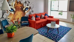 A modern living room with a red sofa set, a coffee table, and a wall mural featuring a cat's face.