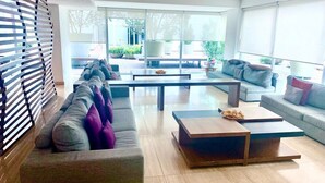 A modern living room with a sectional sofa, two coffee tables, and a large window with blinds.