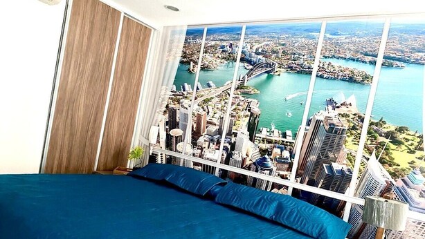 A bedroom with a large bed, a view of a cityscape, and a window with blinds.