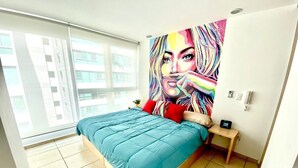A modern bedroom with a large bed, a colorful painting on the wall, and a window with a city view. - 2 BEDROOMS WITH POOL, GYM, 24 HOURS SECURITY, 7 PEOPLE (Guadalajara)