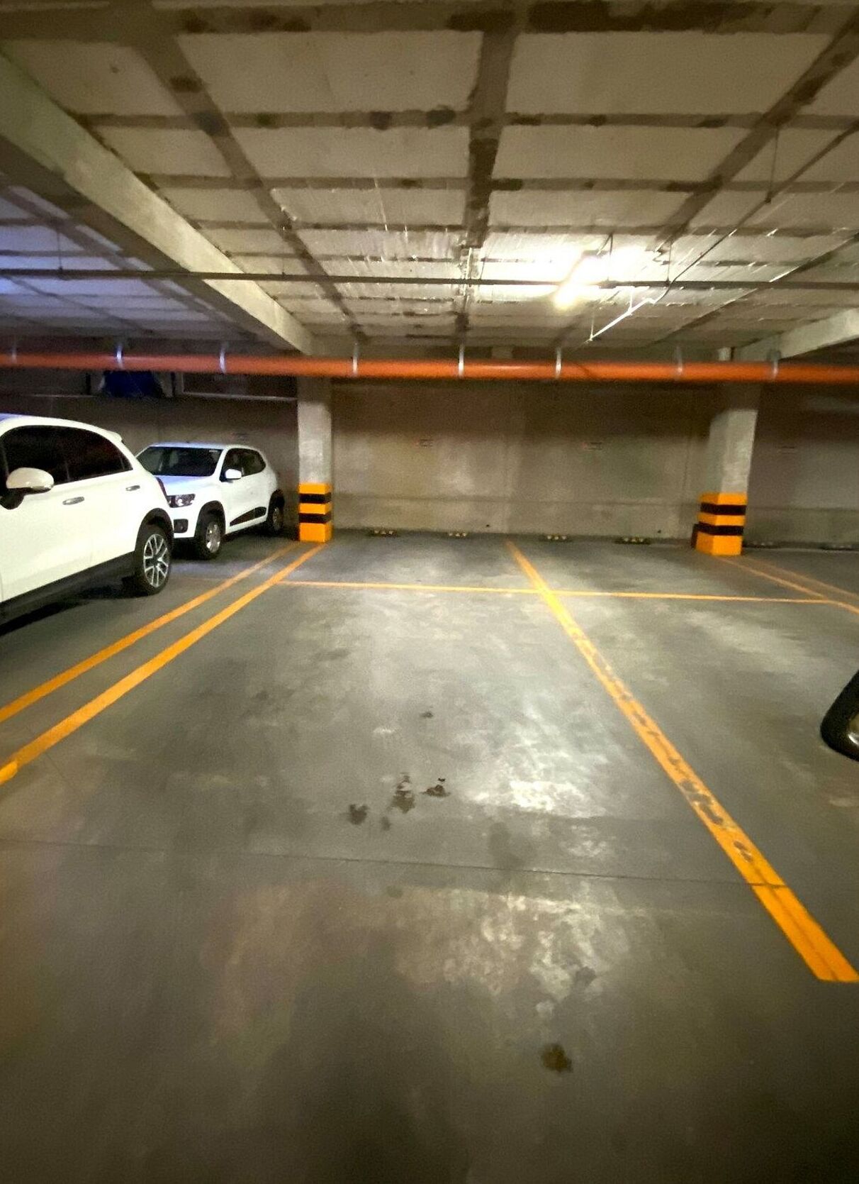 An underground parking garage with concrete walls, yellow parking lines, and two white cars parked.