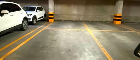 An underground parking garage with concrete walls, yellow parking lines, and two white cars parked.
