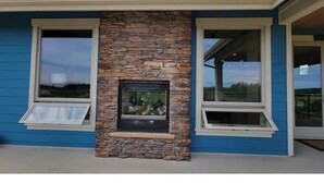 A building with a stone fireplace, two windows with white frames, and a blue exterior. - Executive House Suite with Gorgeous Olympic Views (Port Angeles)