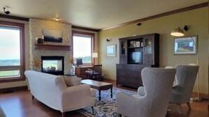 A living room with a fireplace, a television, and a large window overlooking a scenic view. - Executive House Suite with Gorgeous Olympic Views (Port Angeles)