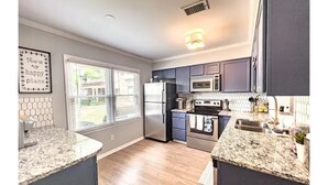A modern kitchen with granite countertops, stainless steel appliances, and a window with blinds. - Beautiful 3 Bedroom Townhouse (Greensboro)